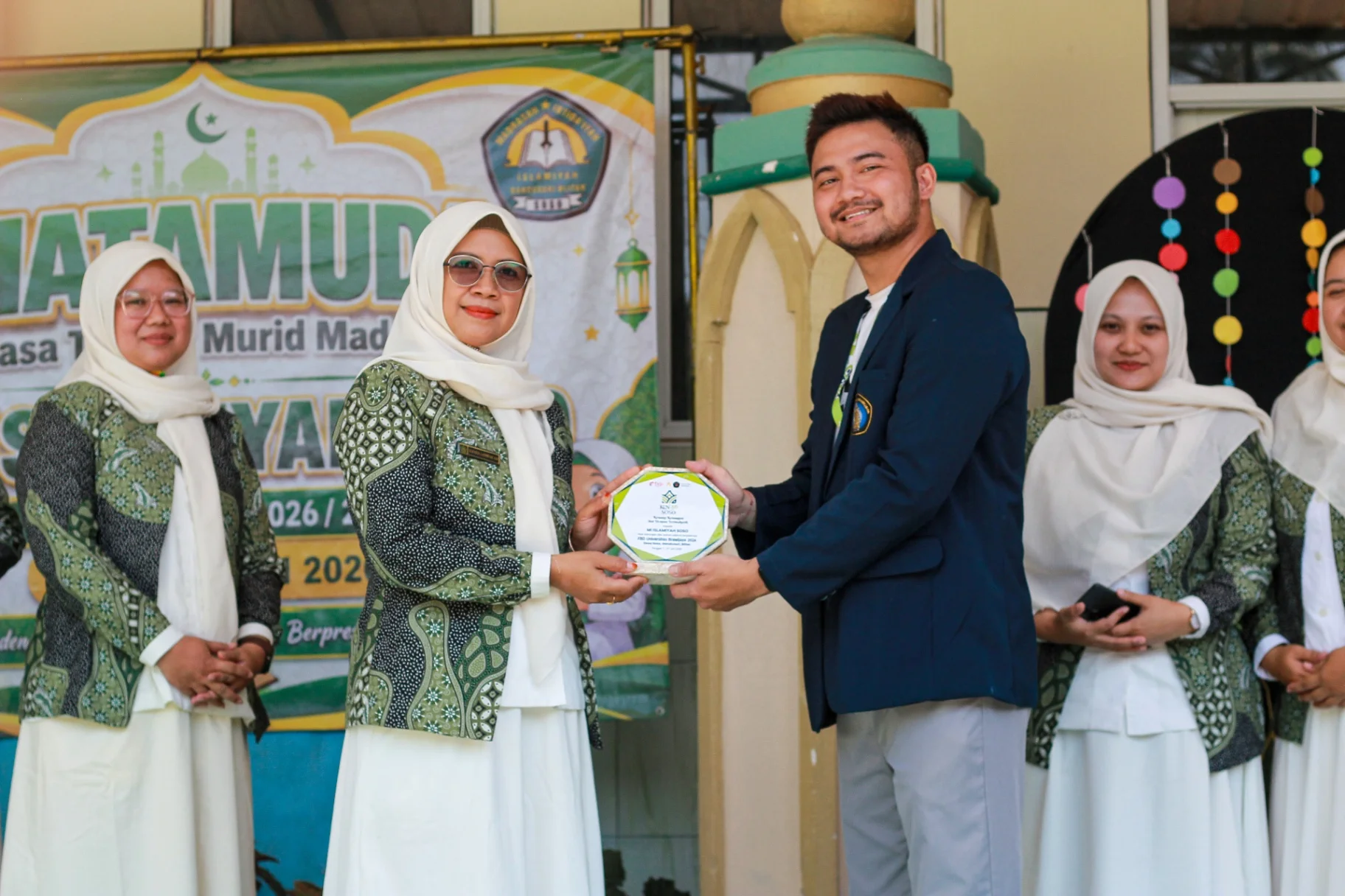 Koordinator Desa FBD Kelompok 56 Universitas Brawijaya menyerahkan plakat kepada Kepala MI Islamiyah Soso sebagai simbol apresiasi dan terjalinnya kolaborasi dalam pelaksanaan Program Generasi Emas pada rangkaian kegiatan MATAMUDA Tahun Ajaran 2026/2027.